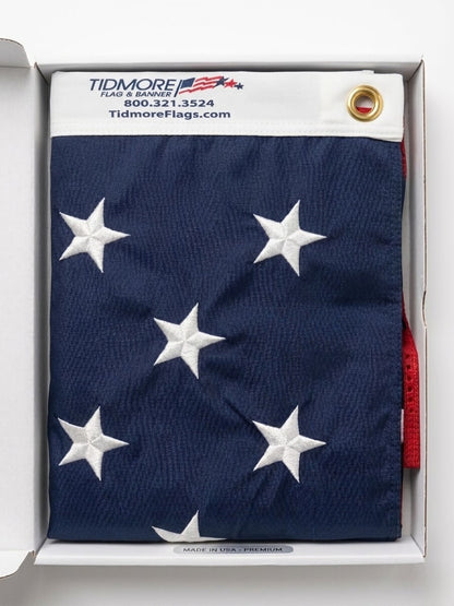 Folded American flag with white stars on a blue background, displayed in a box with Tidmore Flags branding.